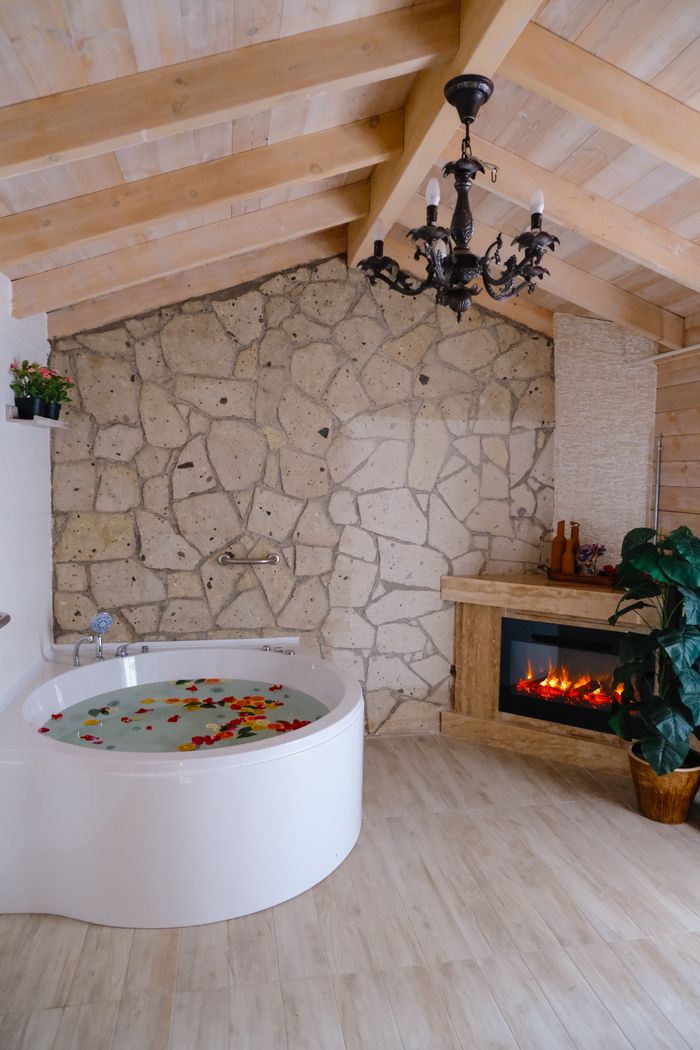 Elegant bathroom featuring a round bathtub, stone wall, and cozy fireplace.