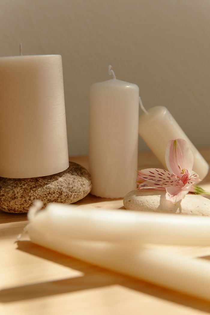 Tranquil setup with white candles, pink flower, and stones on a wooden surface, perfect for relaxation themes.